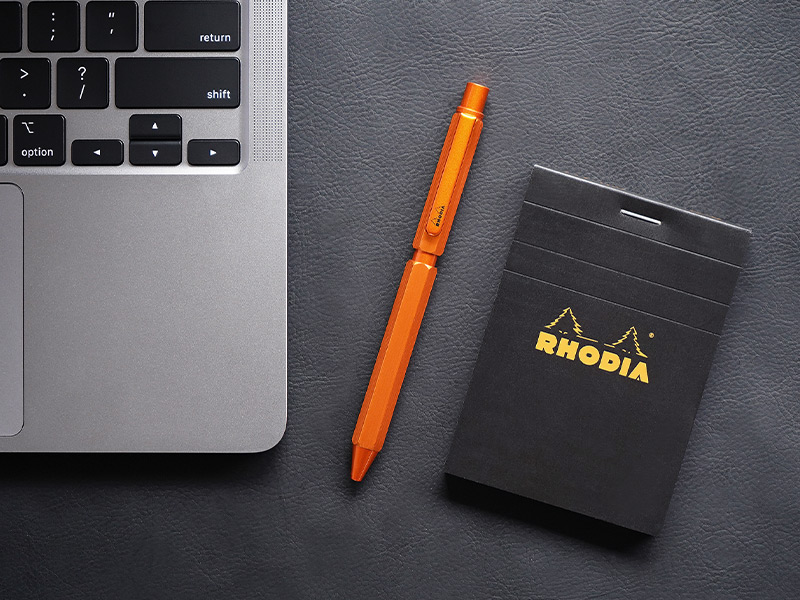 オレンジ色のロディアマルチペンがPC・メモ帳と並んでいる様子