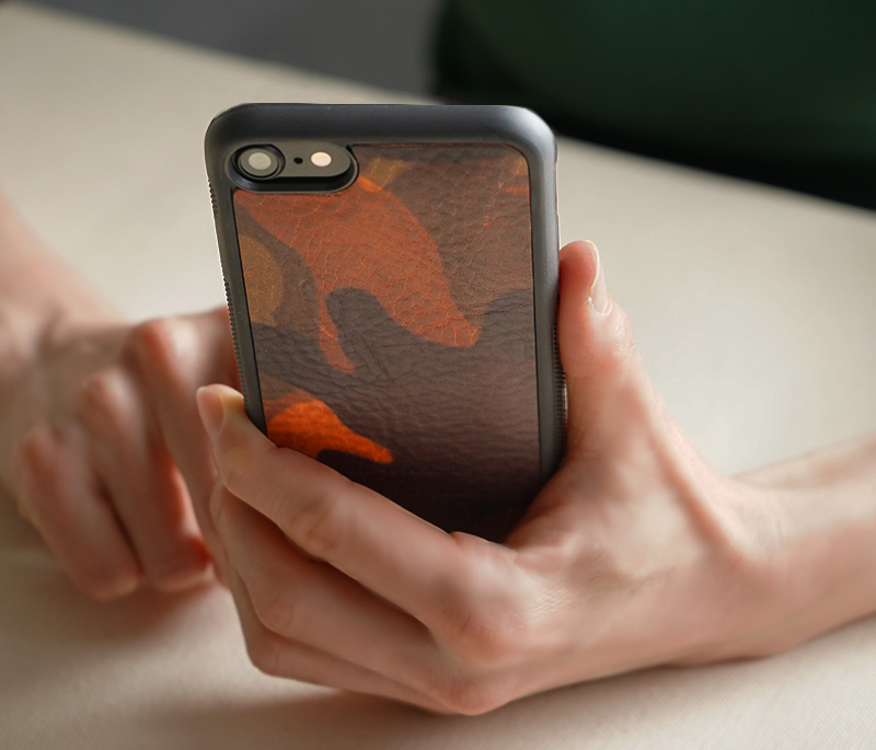 カモフラージュ柄レザー（オレンジ）の背面型ケースを手に持った様子